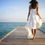 Young woman in white clothes walking on a pier on Maldives